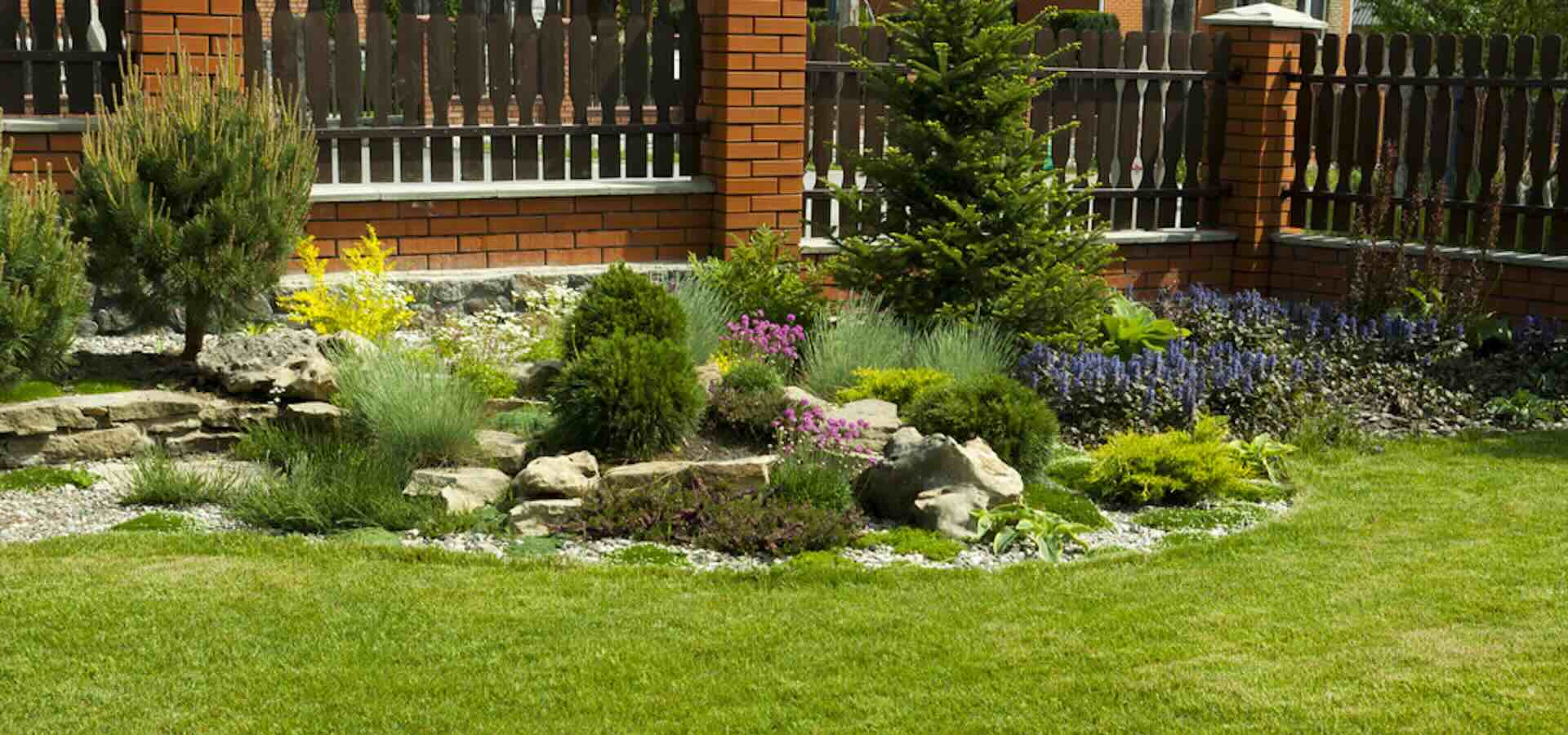 A beautiful landscaped section with flowers, plants, and rocks near a fence.